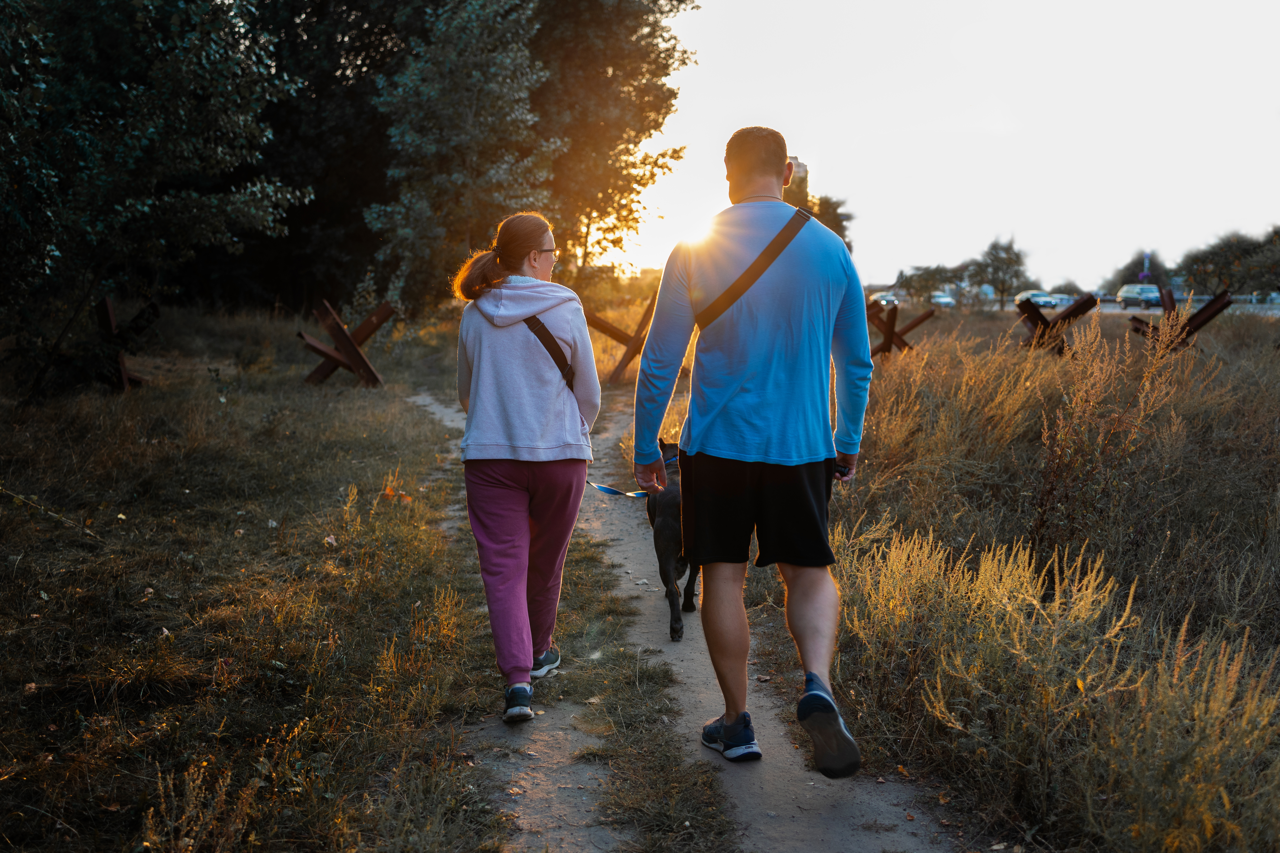 back rear view of couple walking with dog along paving cobblestone pathway